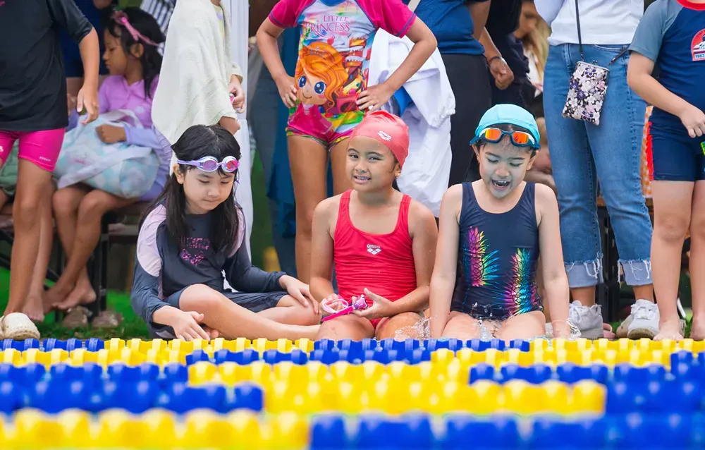 A group of young girls are sitting on the edge of a swimming pool.