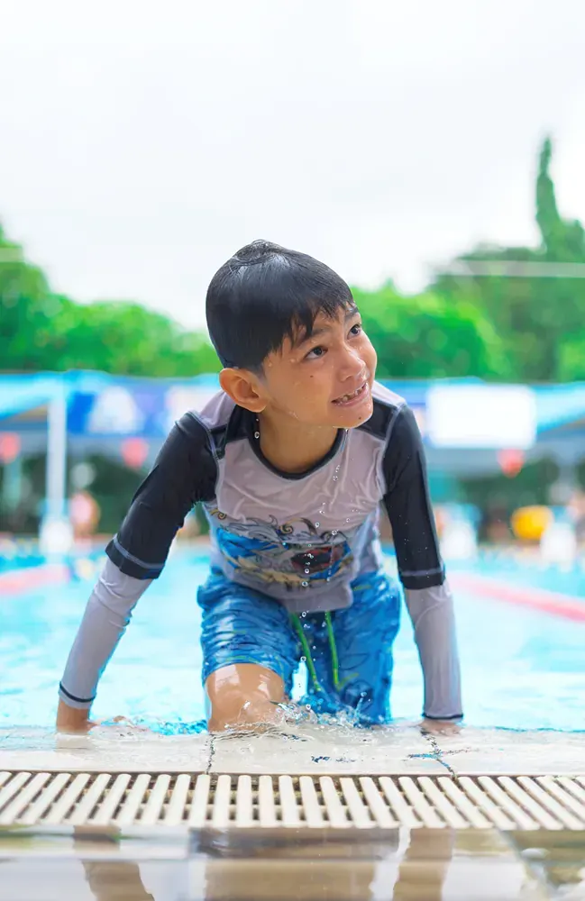 A young boy is crawling out of a swimming pool.