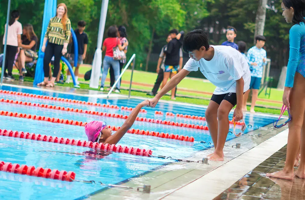 A boy is helping a girl out of a swimming pool.