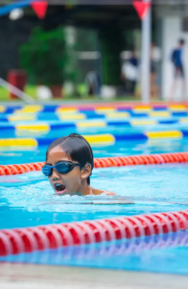 A young girl wearing goggles is swimming in a swimming pool.