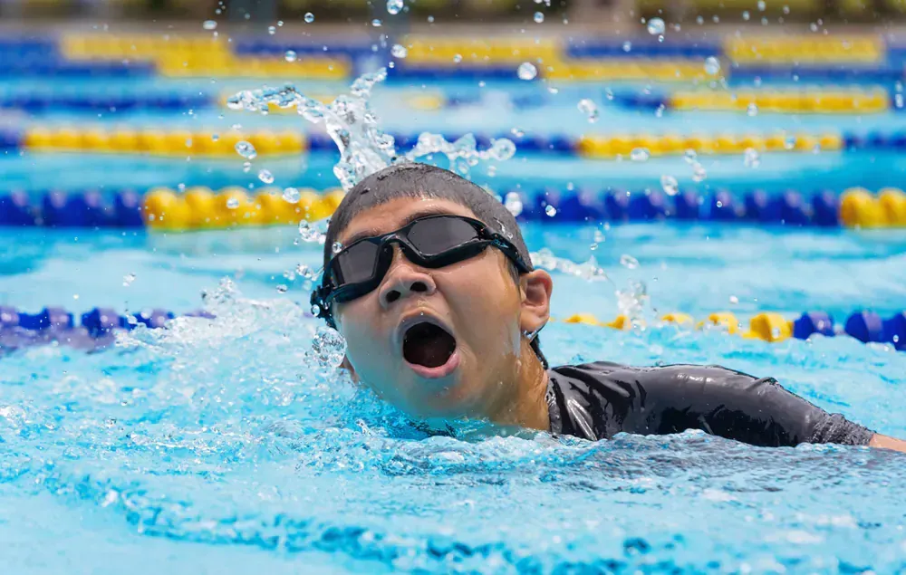 A woman is swimming in a swimming pool with her mouth open.