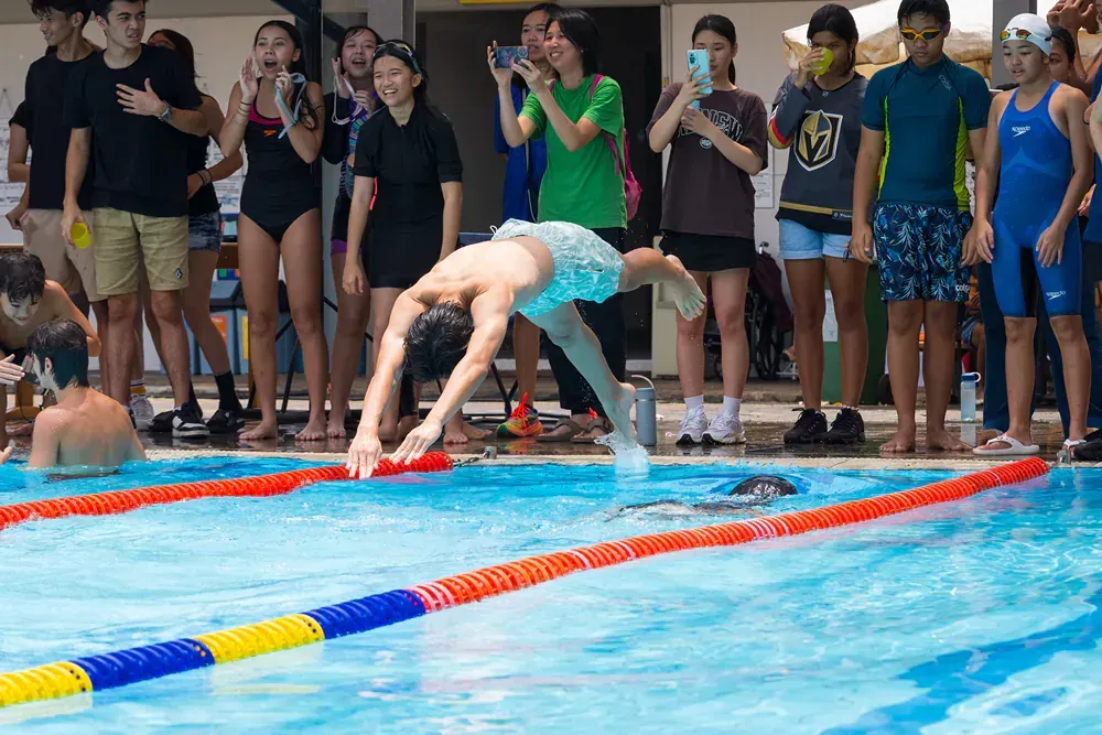 A group of people are watching a man dive into a swimming pool.