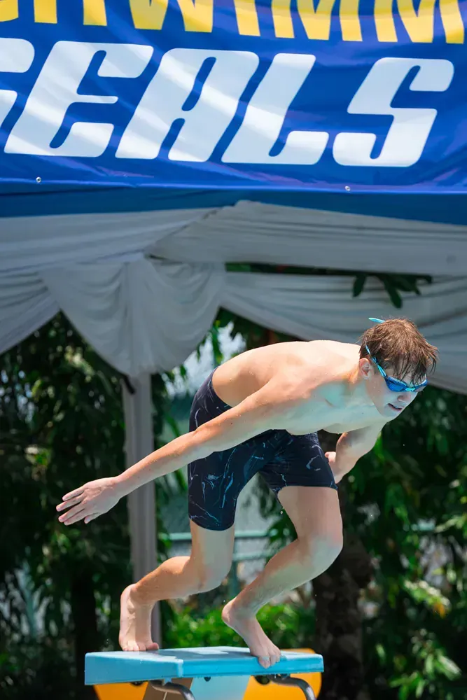 A man is diving into a pool under a sign that says goals