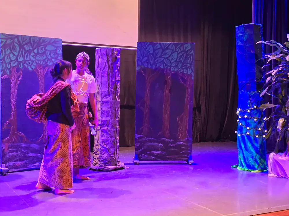 A man and a woman are standing on a stage with purple lights.