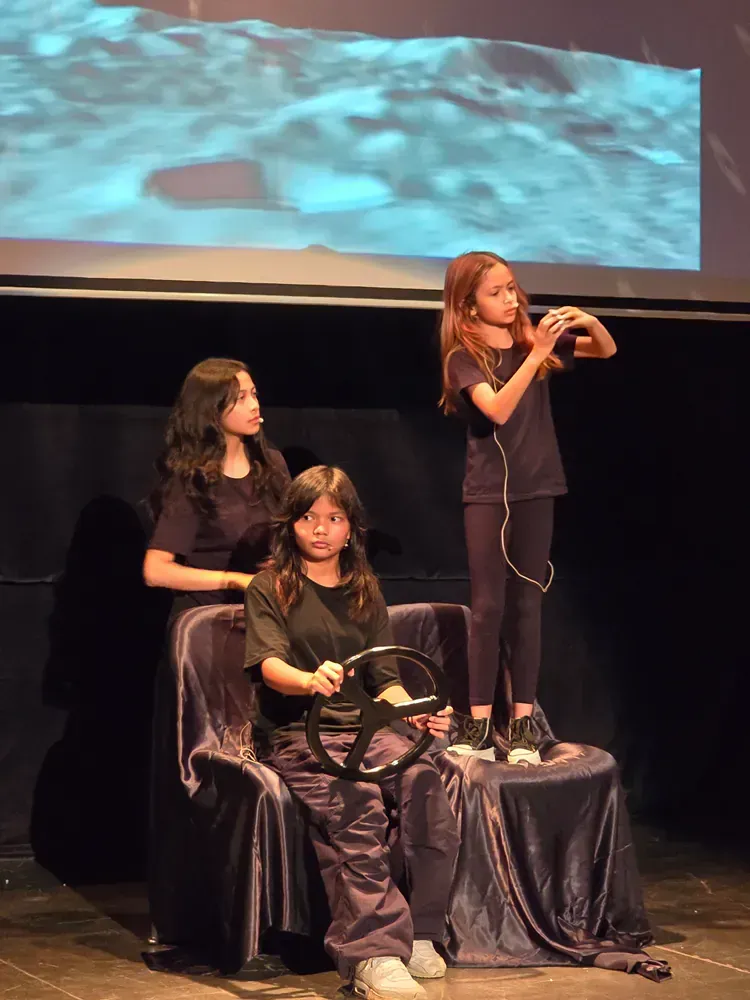 Three young girls are playing a video game on a stage.