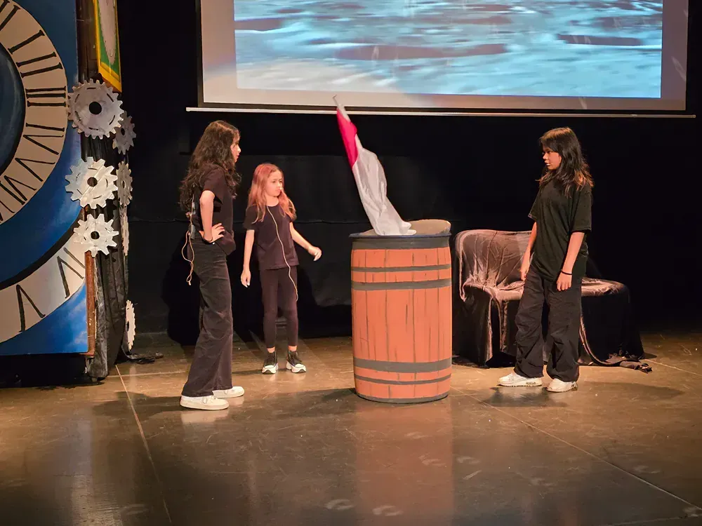 A group of girls are standing around a wooden barrel on a stage.