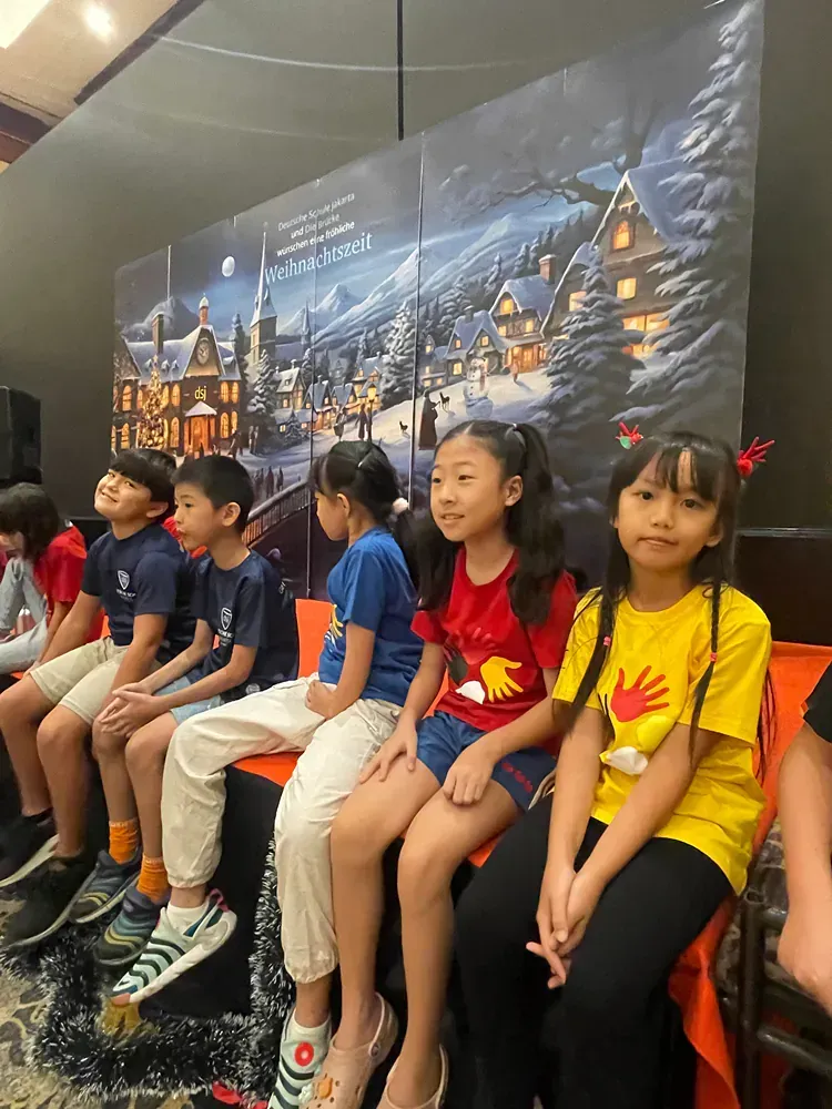 A group of children are sitting on a bench in front of a painting.