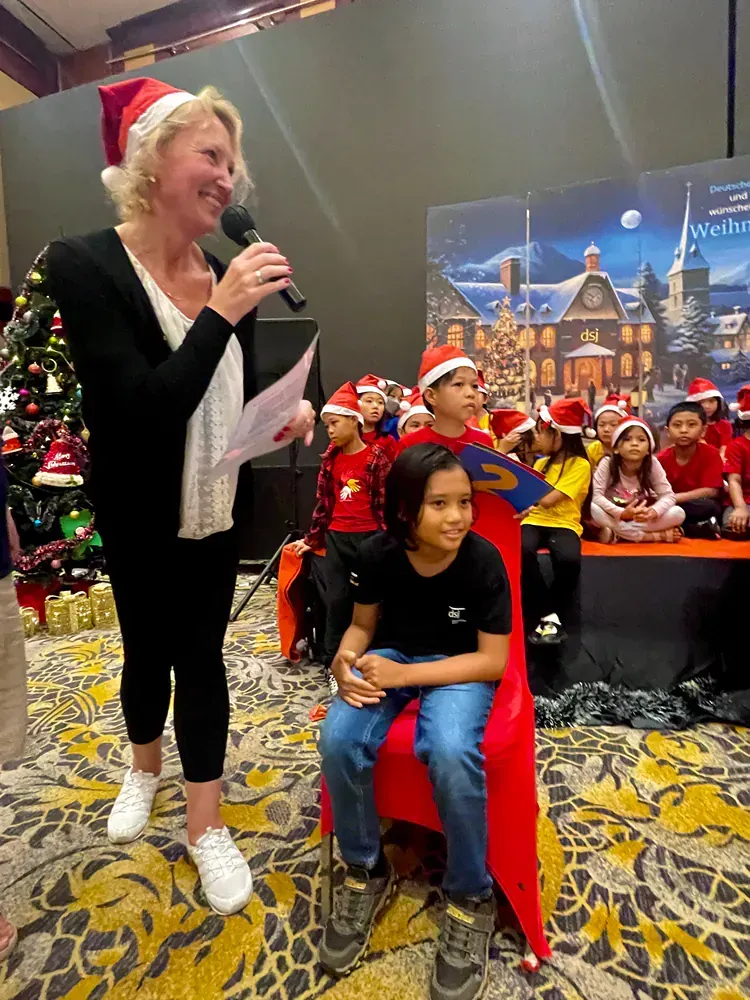 A woman is standing in front of a group of children wearing santa hats.