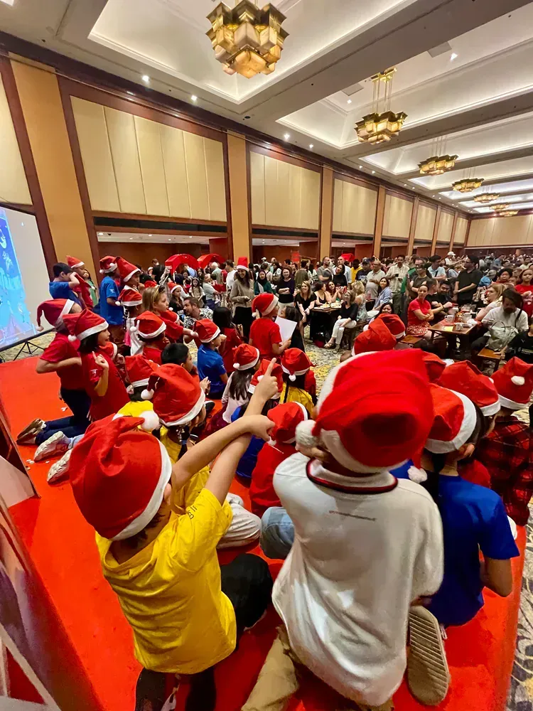 A group of children wearing santa hats are sitting in a large room.