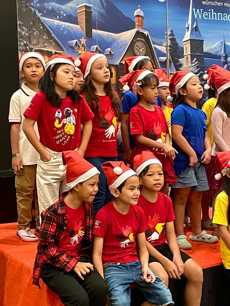 A group of children wearing santa hats are sitting on a stage.