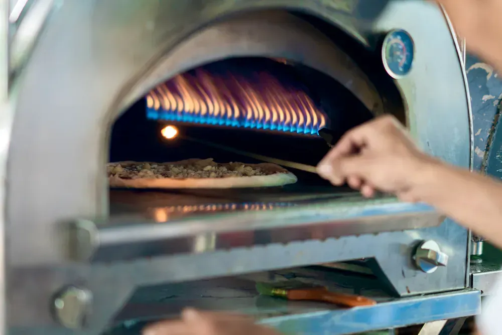 A person is cooking a pizza in a stainless steel oven.