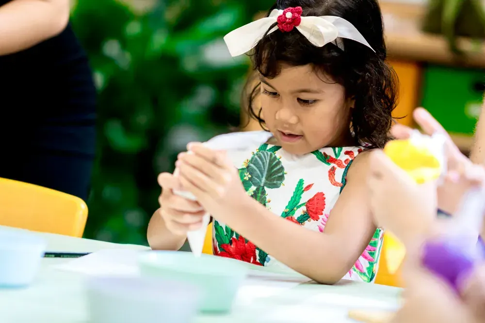 A little girl is sitting at a table playing with glue.