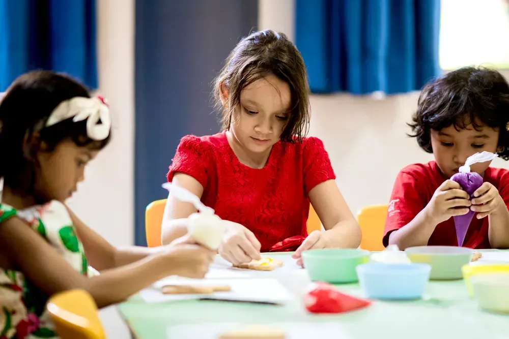A group of children are sitting at a table decorating cookies.