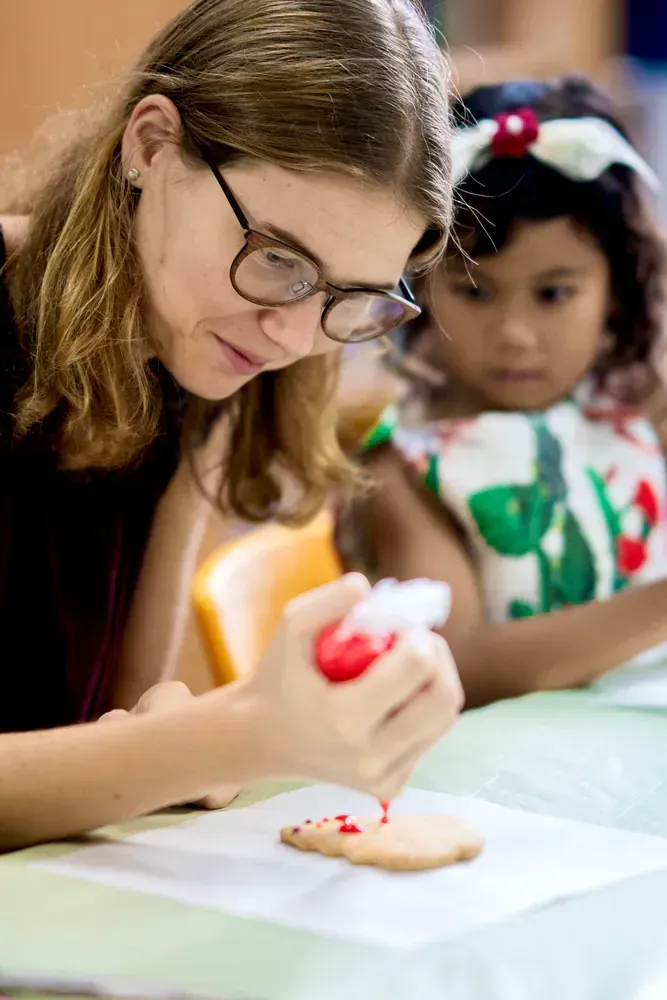 A woman is decorating a cookie with icing while a little girl watches.