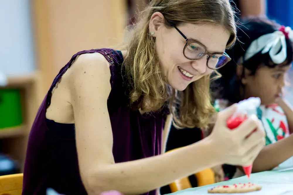 A woman is sitting at a table decorating a cookie with icing.