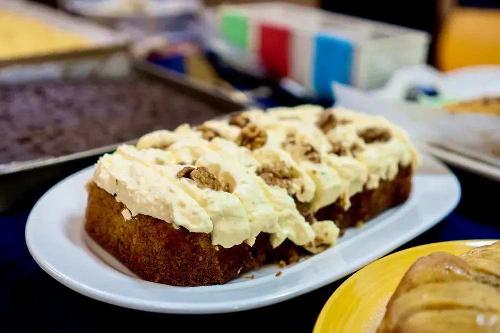 A loaf of carrot cake with cream cheese frosting and walnuts on a white plate.