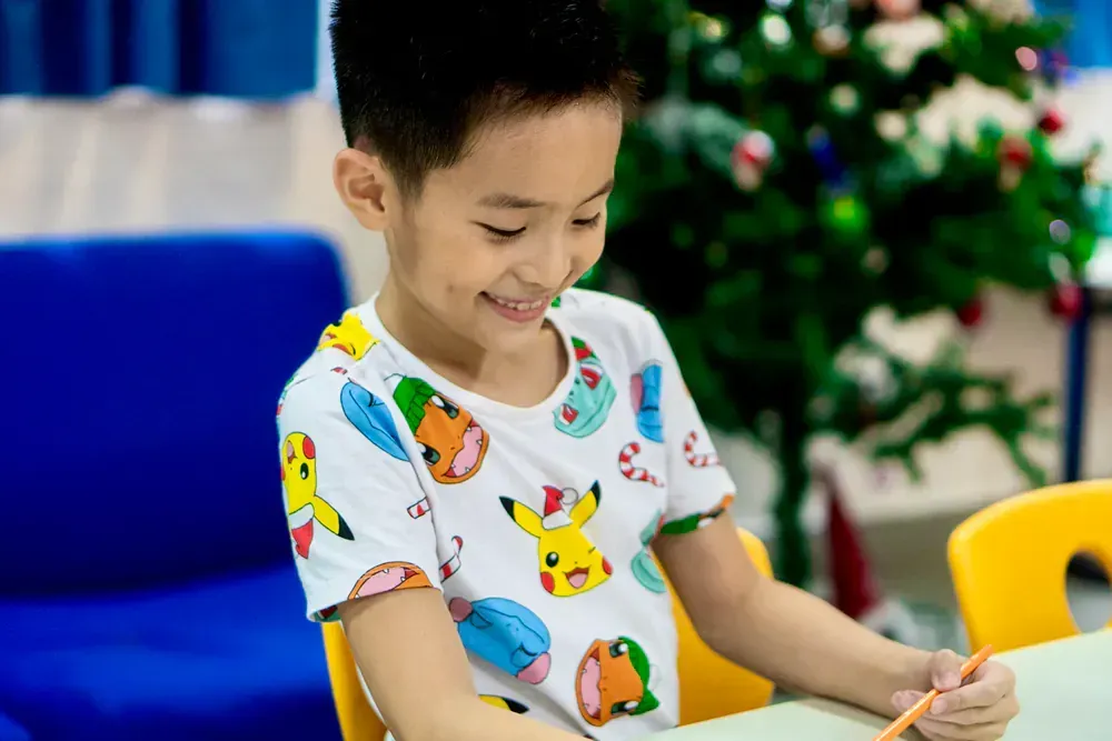 A young boy is sitting at a table with a pencil in his hand.