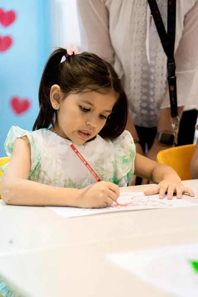 A little girl is sitting at a table drawing with a pencil.