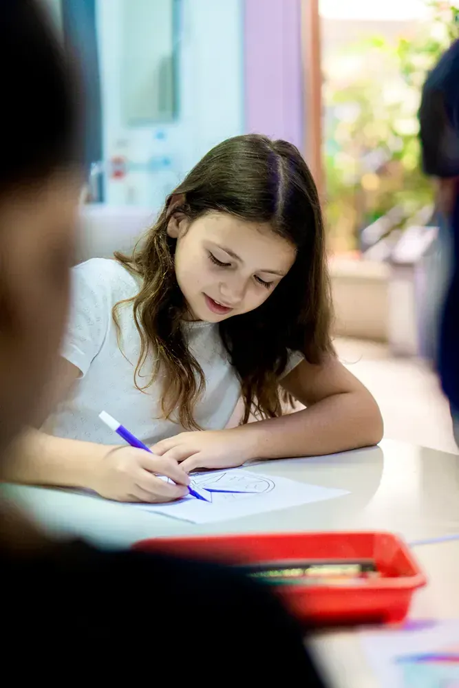 A young girl is sitting at a table writing on a piece of paper.