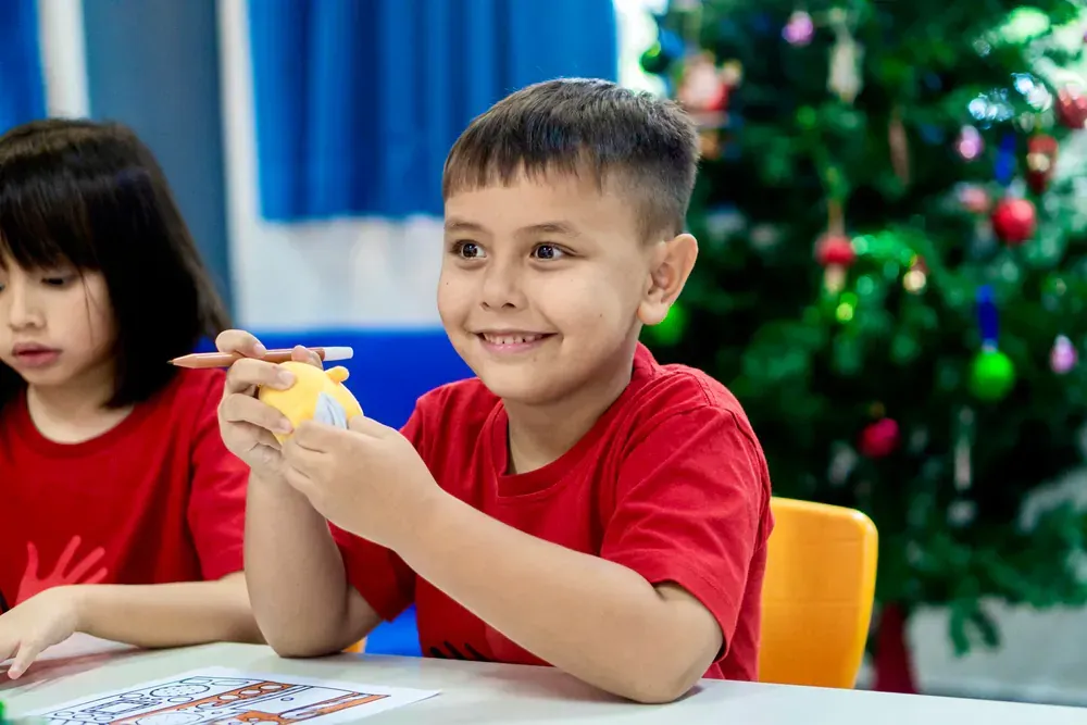 A boy and a girl are sitting at a table with a christmas tree in the background.