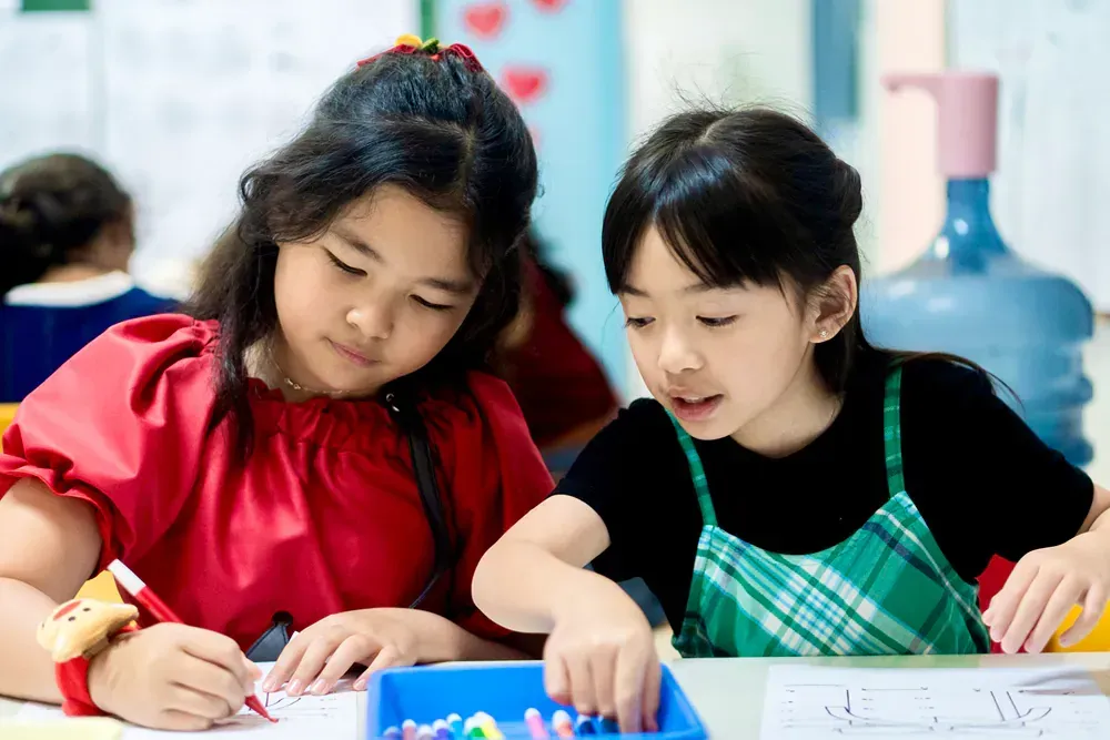 Two young girls are sitting at a table in a classroom.