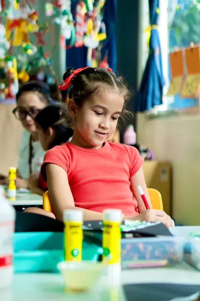 A little girl is sitting at a table in a classroom.