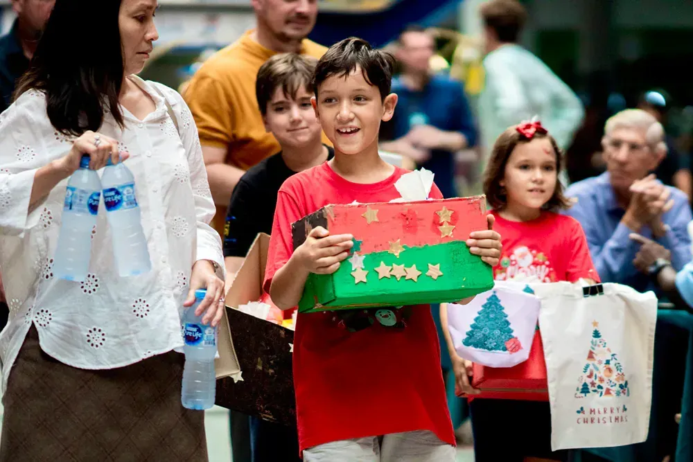 A boy is holding a christmas present in front of a crowd of people.
