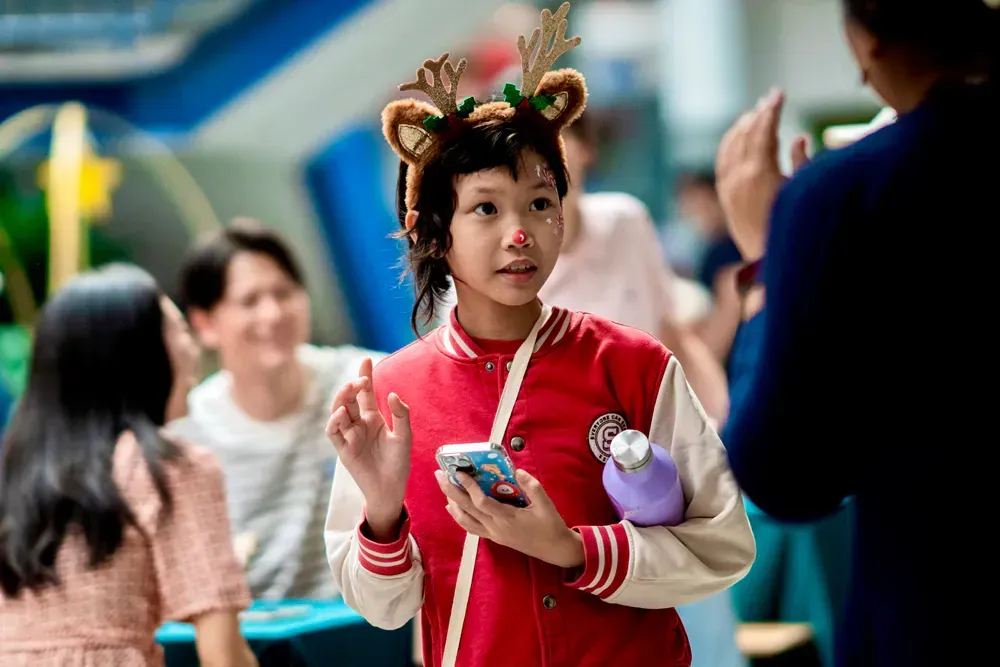 A young girl wearing a reindeer headband is holding a cell phone.