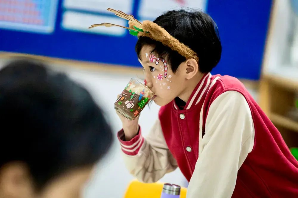 A young boy wearing a reindeer headband is drinking from a cup.