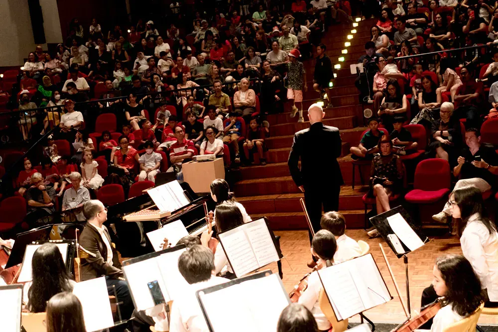 A large orchestra is playing in front of a crowd in an auditorium.