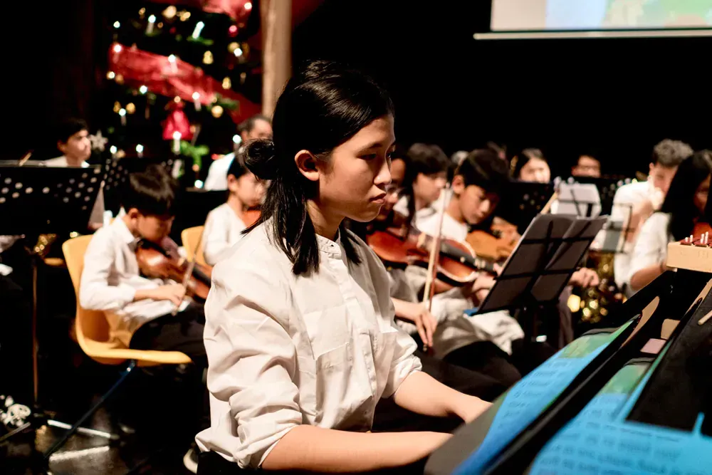 A woman is playing a piano in front of an orchestra.