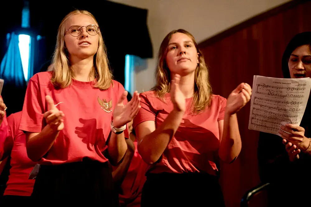 A group of young women in red shirts are singing in a choir.