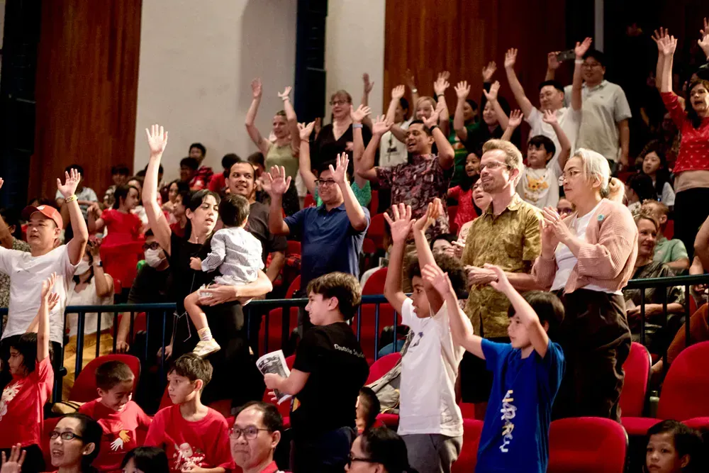 A large group of people are sitting in a stadium with their hands in the air.