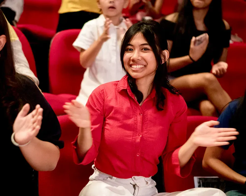 A woman in a red shirt is smiling in a crowd of people
