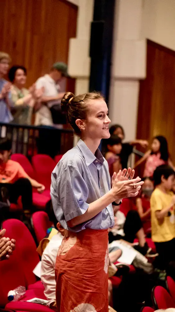 A woman is standing in front of a crowd in an auditorium clapping her hands.