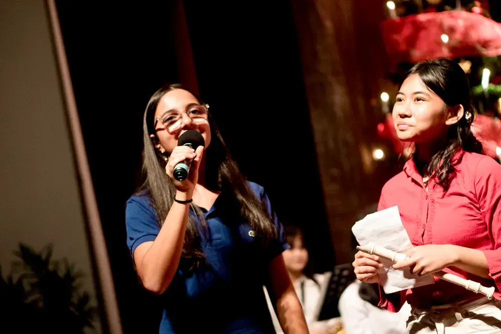 Two women are singing into microphones in front of a christmas tree.