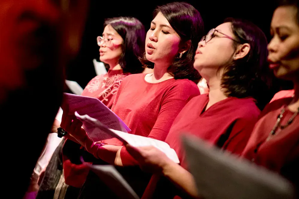 A group of women are singing in a choir on a stage.