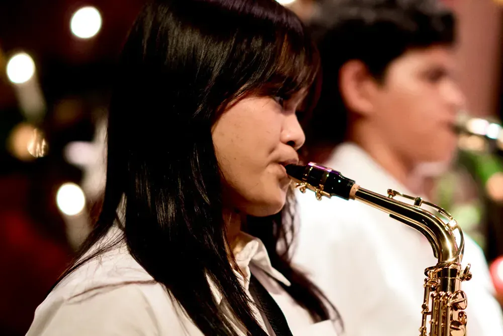A woman is playing a saxophone with a man in the background.