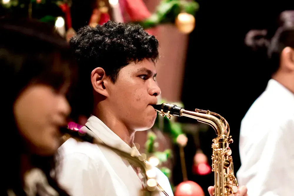 A young boy is playing a saxophone in front of a christmas tree.