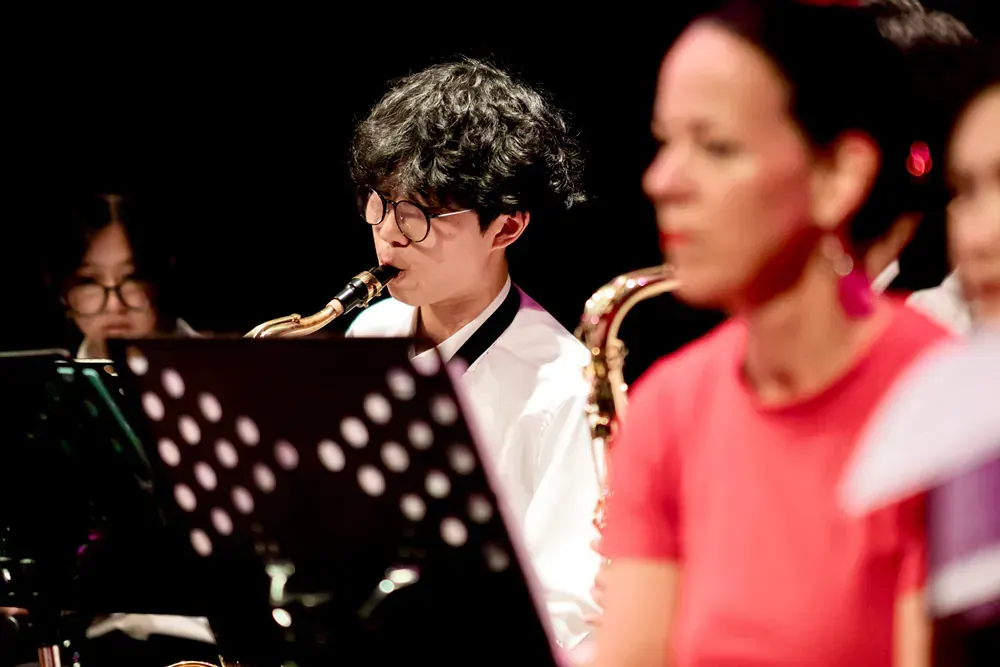 A man is playing a saxophone in an orchestra with other people.