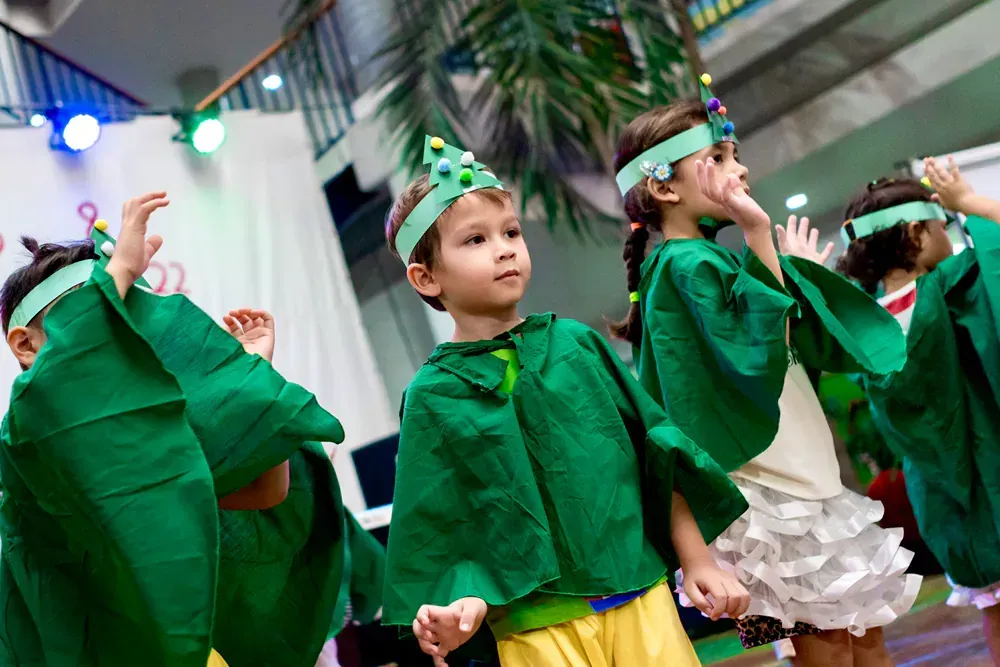 A group of children dressed in green costumes are dancing on a stage.