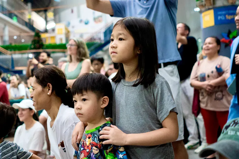 A girl and a boy are standing in front of a crowd of people.