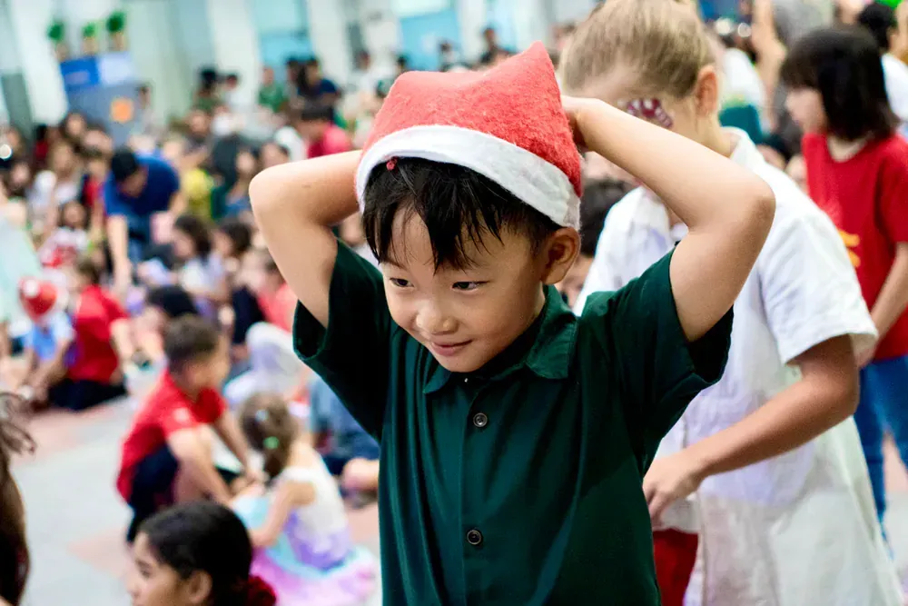 A boy wearing a santa hat is standing in front of a crowd of children.