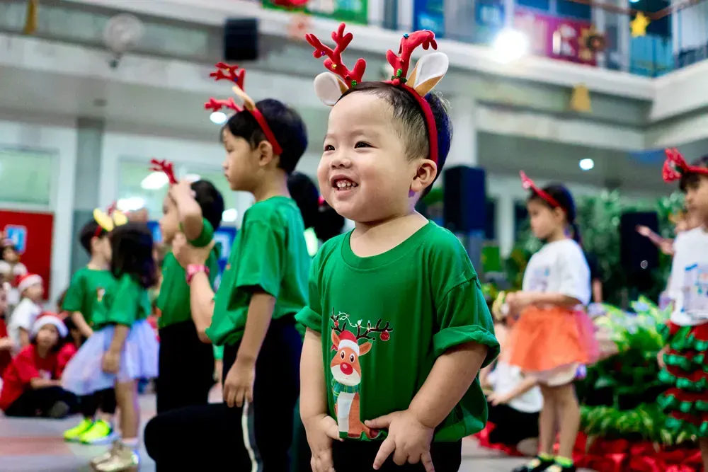 A group of children wearing reindeer antlers are dancing at a christmas party.