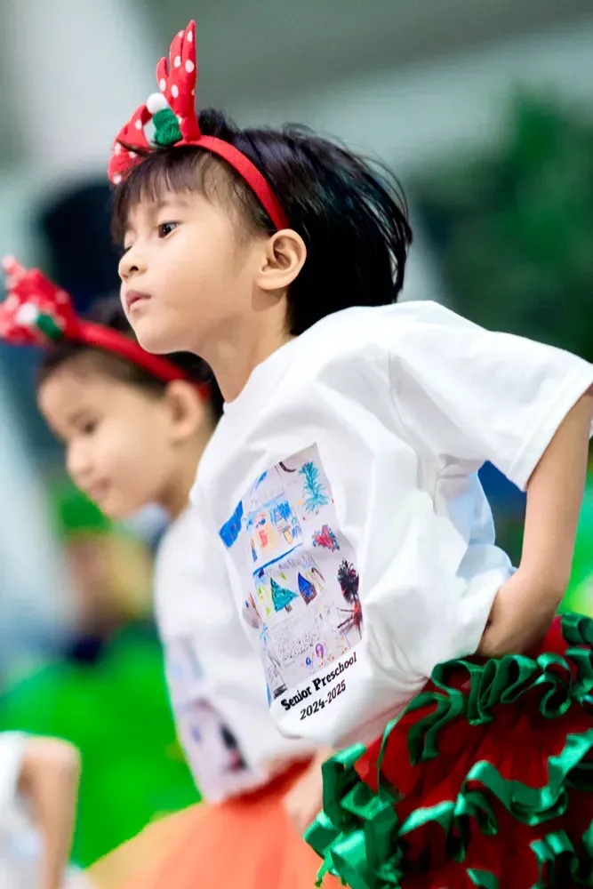 A little girl wearing a headband and a skirt is standing next to another little girl.