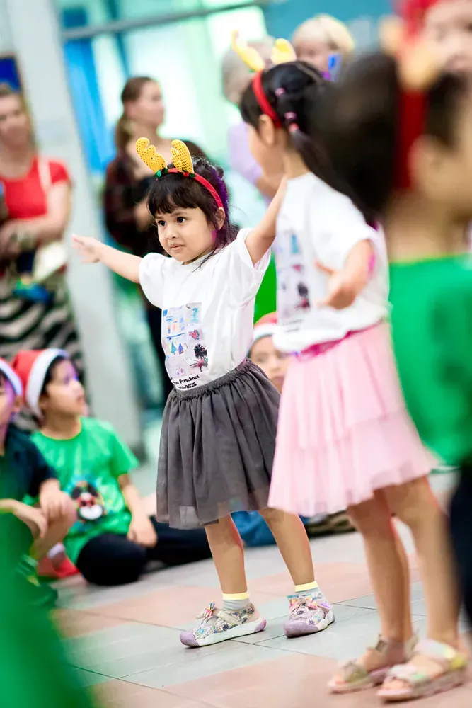 Two little girls are dancing in front of a crowd of children.