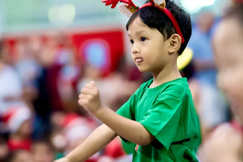 A young boy wearing reindeer antlers and a green shirt is dancing.