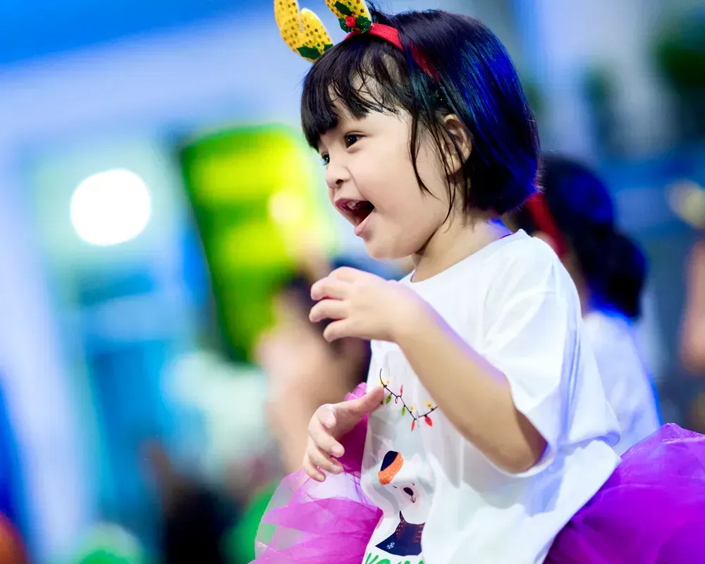A little girl wearing a headband and a tutu is smiling.