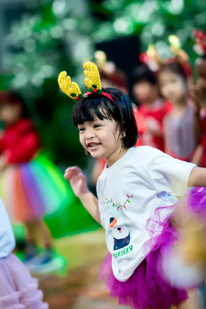 A little girl wearing a purple tutu and antlers is dancing in front of a group of children.
