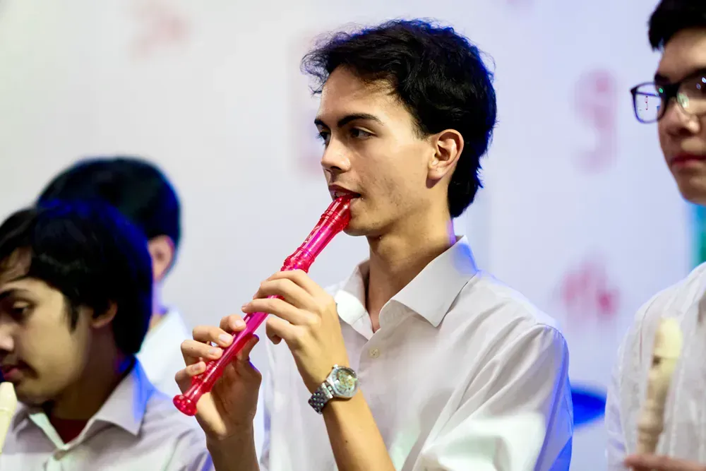 A young man is playing a pink recorder in a band.